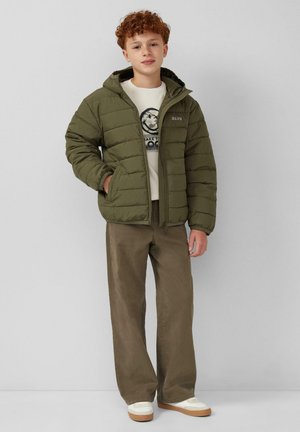 Olijfgroen donsjack met capuchon, twee zijzakken en een logo. Gecombineerd met een beige sweatshirt met ronde hals en bruine broek met wijde pijpen.