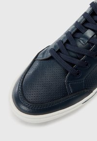 Marineblå lærersneakers med perforert design, flate lisser og hvit gummisåle. Strukturerte detaljer på overdel og sidepaneler.