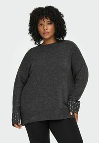 Preveliki sivi pulover od mekog pletiva, s rebrastim manžetama ukrašenim dekorativnim metalnim detaljima. Opusten kroj i okrugli izrez.