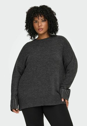 Kolgrå oversized tröja i mjukt stickat material, med ribbade ärmslut och dekorativa nitar. Avslappnad passform och rundad halsringning.