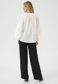 Blusa blanca texturizada con mangas abullonadas, ceñida en la muñeca; combinada con pantalones anchos negros; tejido suave y ajuste relajado.