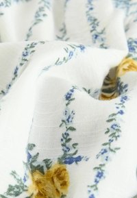 Tissu blanc à texture douce avec un motif floral de roses jaunes et de petites fleurs bleues en rayures verticales.