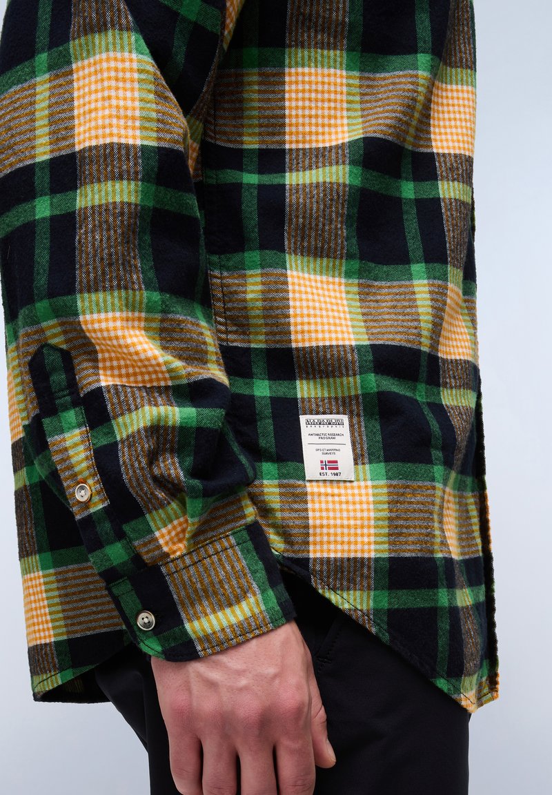 Chemise à carreaux verte, jaune et noire, avec des poignets boutonnés, une fente sur le côté et une étiquette avec les détails de la marque sur le bas devant.