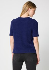 Marineblå, fluffy kortærmet sweater med rund hals og en afslappet pasform. Blød tekstur med en glat finish, båret med mørke jeans.