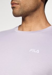 Světle fialové tričko Fila s kulatým výstřihem a krátkými rukávy. Na levém prsu je malé bílé logo. Hladká textura.