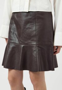 Donkerbruine leren rok met uitlopende zoom, gedragen met een wit shirt met lange mouwen, toont mid-dij lengte.