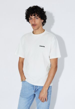 T-shirt en coton blanc à manches courtes, avec un petit logo noir "Ddenim" sur la poitrine. Jeans en denim bleu clair avec une coupe décontractée.
