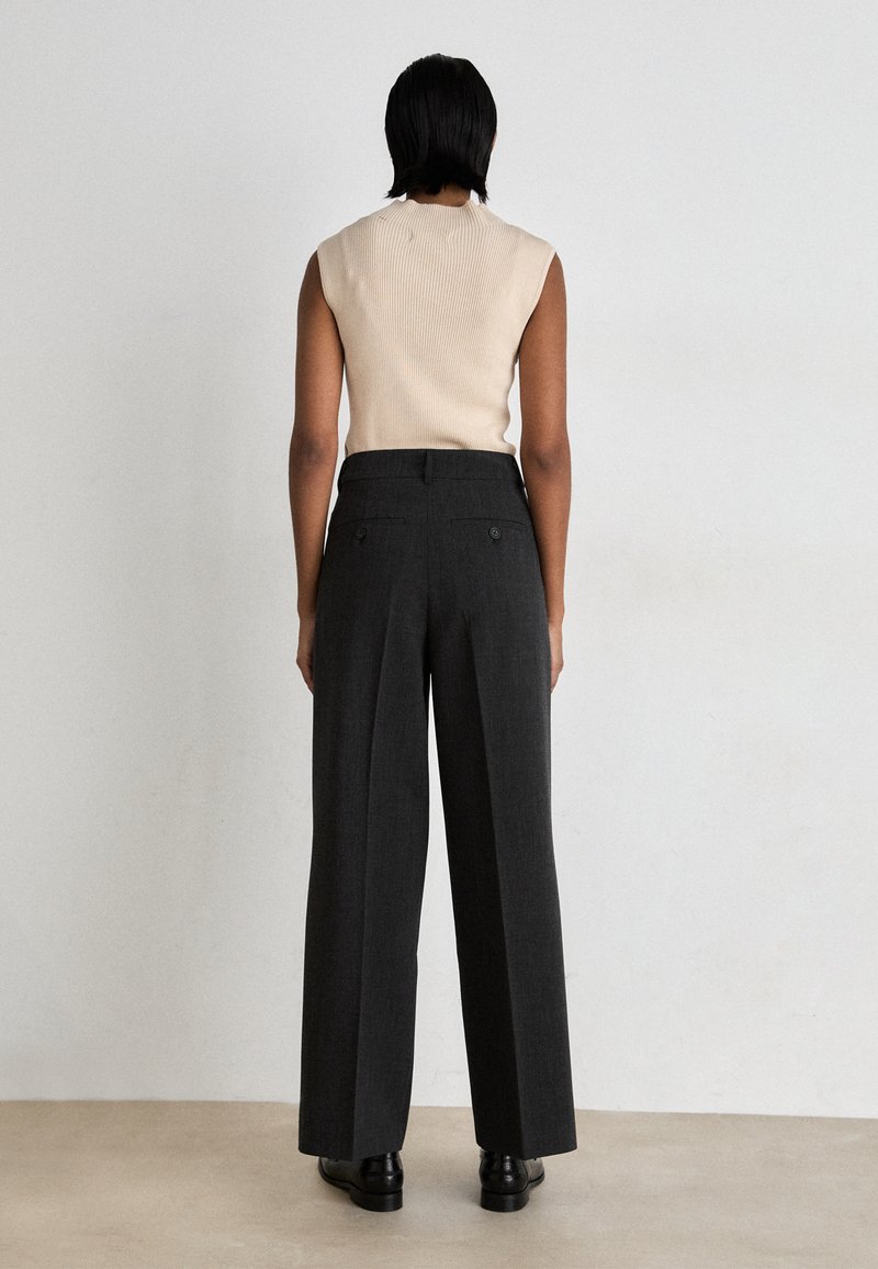 Beige geripptes ärmelloses Top, kombiniert mit hoch taillierten, weit geschnittenen grauen Hosen mit knöpfbaren Gesäßtaschen und einer glatten Stoffstruktur.