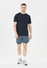 Marineblå atletisk T-shirt med korte ærmer, kombineret med lysegrå shorts. Har åndbart stof og minimalistisk design. Hvide sneakers sættes i fokus i outfittet.