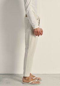 Pantalon en denim clair à coupe droite, doté d'un zip et de cinq poches, avec une finition texturée subtile, complété par des tongs blanches.