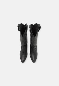 Bottes de cowboy en cuir noir avec un nez pointu, présentant des détails embossés sur la tige et des languettes pour un enfilage facile.