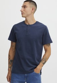Námorně modré tričko s krátkým rukávem typu henley s třemi knoflíky u výstřihu, vyrobené z bavlny, s hladkou texturou a uvolněným střihem.