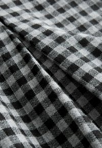 Sort og gråt ternet stof med hundetandsmønster; blød tekstur med en let glans, der har skiftende store og små firkanter.