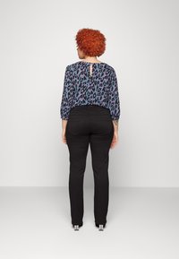 Pantalones ajustados negros combinados con una blusa azul de estampado de leopardo que cuenta con mangas de tres cuartos y un detalle de abertura en la espalda.