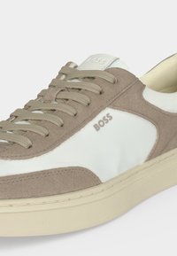 Baskets en daim blanc et beige avec des lacets beiges, une semelle crème et le logo « BOSS » sur le côté et la languette.