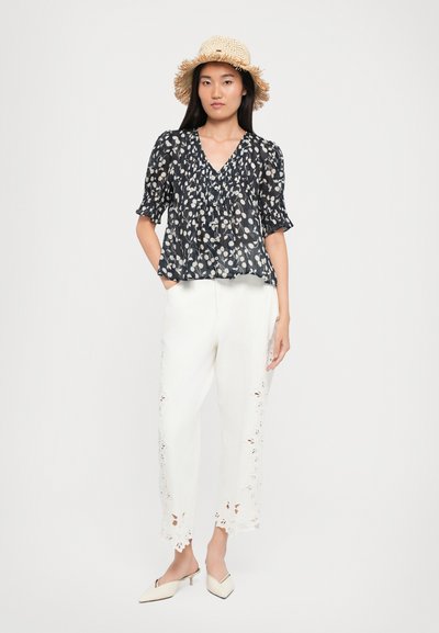 Marineblaue Bluse mit kurzen Puffärmeln, kombiniert mit weißen Hosen mit Spitzenverzierungen am Saum, ergänzt durch einen Strohhut.