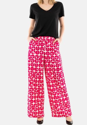Pantaloni a gamba larga con un motivo geometrico rosa e bianco, realizzati in tessuto leggero. Abbinati a una t-shirt nera a scollo a V, con tasche laterali.