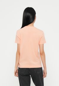 Peach short-sleeve t-shirt with a crew neckline, made of soft fabric. Features simple design and a relaxed fit, paired with dark gray pants.