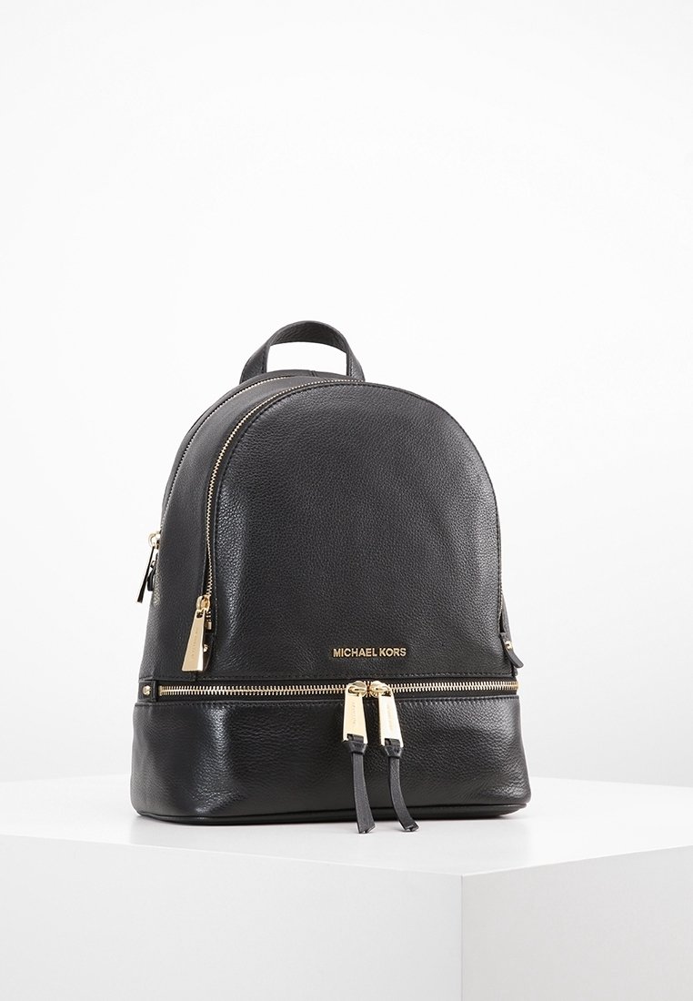 Sac à dos en cuir noir Michael Kors avec fermetures éclair dorées et logo, exposé sur une surface blanche sur fond blanc uni.