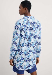 Camicia a maniche lunghe con una stampa di foglie blu e azzurro su uno sfondo chiaro. Tessuto morbido con colletto a camicia e piega sul retro.