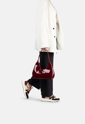Sac à main en cuir verni bordeaux avec une silhouette courbée, des poignées courtes et une finition brillante. Porté avec un pantalon à rayures noires et des baskets.