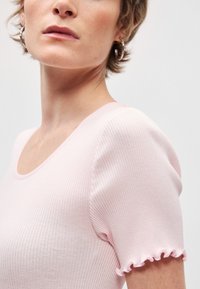 Ροζ ριμπ κορυφή με στρογγυλή λαιμόκοψη και κοντά μανίκια που διαθέτει φρουφρού τελείωμα. Το ύφασμα φαίνεται μαλακό με εφαρμοστή σχεδίαση.