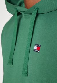 Felpa verde con finitura testurizzata, dotata di cordini e un piccolo logo ricamato in rosso, bianco e blu sul petto.
