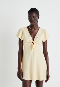 Short yellow dress with a deep V-neck, tie detail at the center, and short flutter sleeves. The fabric has a subtle texture.