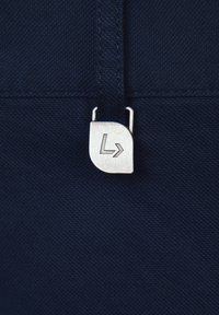 Granatowa tkanina z metalowym suwakiem w kolorze srebrnym, na którym znajduje się częściowe logo i wzór strzałki. Tekstura jest gładka, z delikatnymi detalami przeszycia.