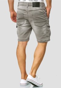 Grijze cargoshorts met meerdere zakken, een gladde textuur en contrasterende stiksels. Draag met witte sneakers en een zichtbare taillebandlabel.