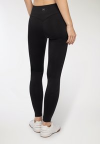 Czarne legginsy z wysokim stanem, o bezszwowym fasonie i subtelnych detalach w szwie. Noszone z białymi butami sportowymi.