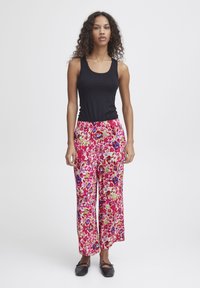 Débardeur noir associé à un pantalon large orné d'un motif floral vibrant en rose, bleu et vert. Tissu lisse, taille élastique.