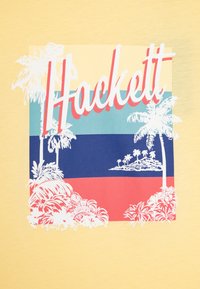 T-shirt jaune avec un graphisme portant le mot "Hackett" en rouge, sur fond multicolore agrémenté d'illustrations de palmiers.