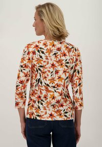 Bloemmotief top met driekwart mouwen, voorzien van oranje, rode en zwarte bloemen op een crèmekleurige achtergrond. Zachte stof, getailleerd ontwerp.