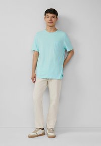 Lichtblauwe t-shirt met korte mouwen en een borstzak, gecombineerd met crèmekleurige broek en beige sneakers. Glad stoftextuur.