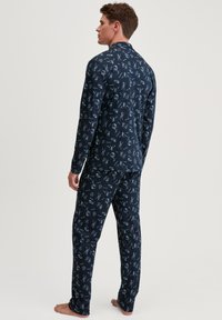 Navyblauw pyjama-set gemaakt van zachte stof, met een patroon van witte tekeningen van gereedschappen en objecten. Langsleeve top en bijpassende broek.