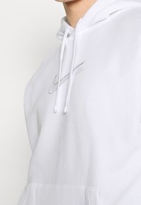 Vit huvtröja i mjukt tyg med en liten, ton-i-ton Nike-logga på bröstet, justerbara dragsnören och en framficka.