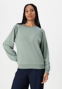 Sudadera verde de manga larga, con un diseño texturizado en forma de V en el frente y puños y dobladillo acanalados. Corte relajado.