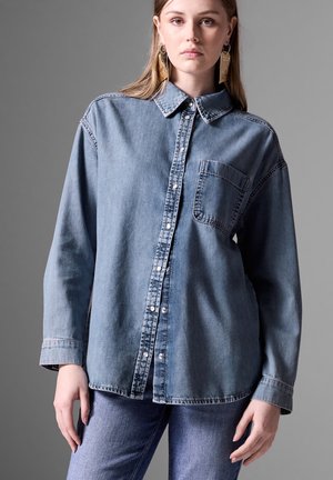 Jeanshemd in Hellblau, mit Knopfleiste und Kragen, einer einzelnen Brusttasche, langen Ärmeln und sichtbaren Nähten.