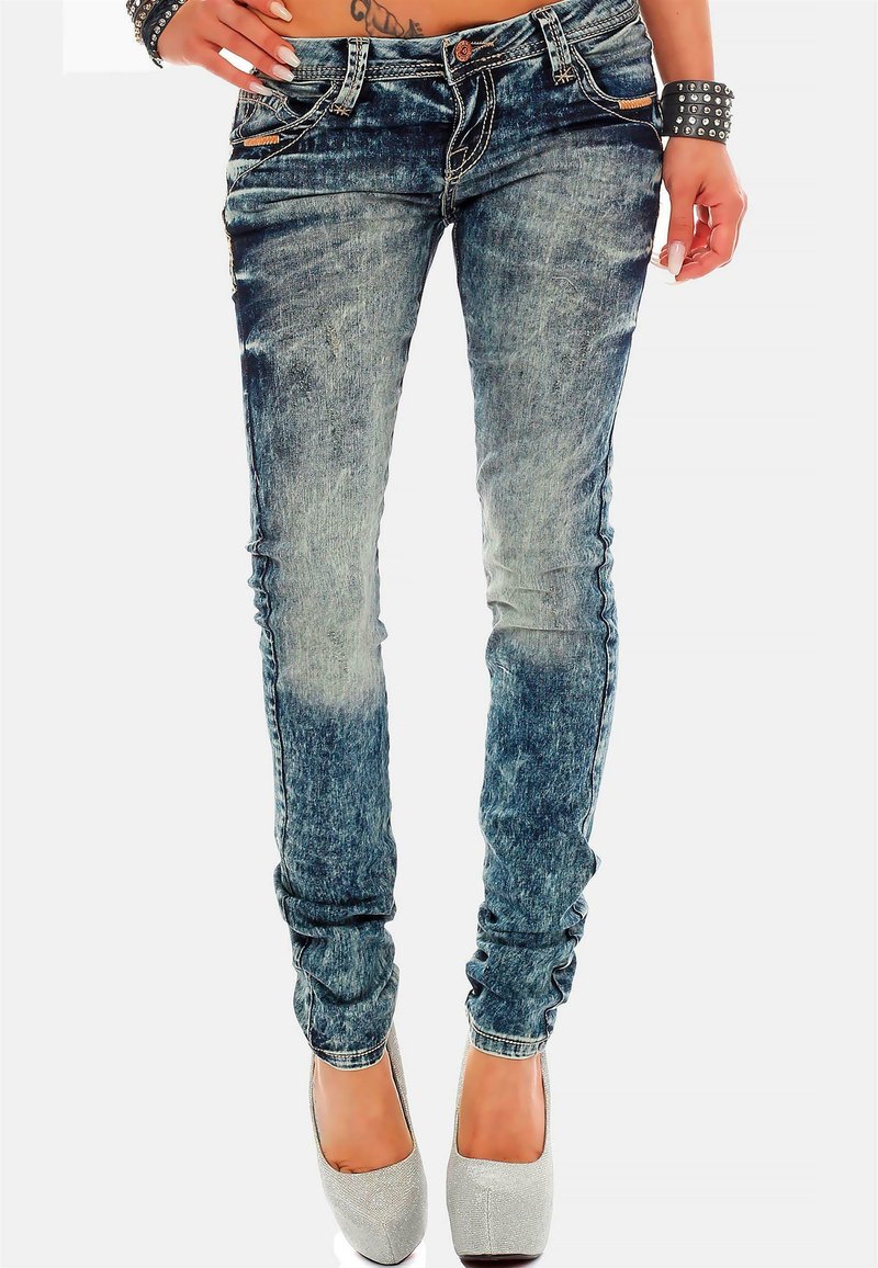 Jeans in denim blu snello con un motivo di scoloritura. Presentano dettagli strappati e una vita a media altezza. Abbinati a tacchi argentati.