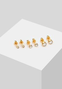 Boucles d'oreilles clous en ton or, comprenant trois paires de tailles variées avec des accents de cristal clair. Texture lisse et design minimaliste.