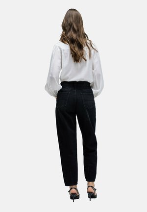 Jeans negros de tiro alto con un corte relajado, que cuentan con dos bolsillos traseros y detalles de costura sutiles, combinados con una blusa blanca de manga larga.