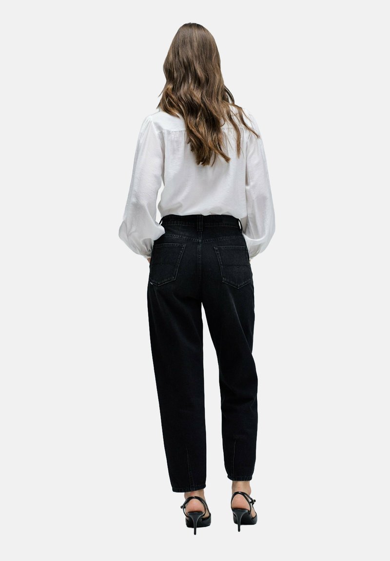 Jeans negros de tiro alto con un corte relajado, que cuentan con dos bolsillos traseros y detalles de costura sutiles, combinados con una blusa blanca de manga larga.