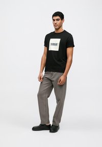 T-shirt preta de manga curta com um gráfico quadrado branco e texto, combinada com calças cinza de corte relaxado e ténis pretos. Estilo simples e casual.