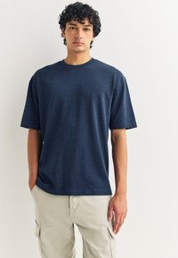 Tumesinise lühikeste varrukatega t-särk, mis on valmistatud pehmest tekstuurist, omab ümarsuud, lahtist lõiget ning minimalistlikku disaini ilma mustrite või aktsentideta.