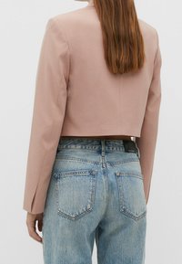 Cropped, light pink blazer made of smooth fabric, paired with high-waisted blue denim jeans featuring classic back pockets and a faded texture.