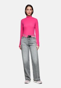 Enger rosa Rollkragenpullover, grau hoch taillierte weit geschnittene Jeans mit kontrastierenden Seitennähten, schwarzer Gürtel und hellfarbige Sneakers.