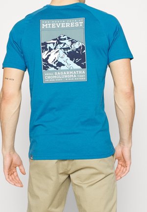 Mand iført blå t-shirt med bjerggrafik og tekst, der henviser til Mt. Everest, Nepal, Tibet og højde på bagsiden.