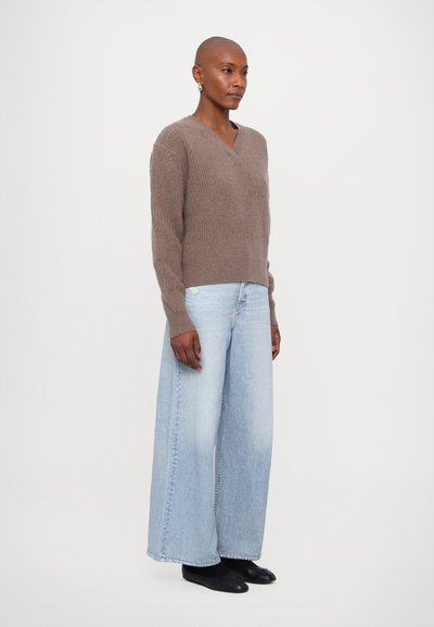Hellbraunes Strickpullover mit V-Ausschnitt, kombiniert mit weiten, hellblauen Jeans und schwarzen Schuhen. Einfaches Design, strukturierter Stoff.