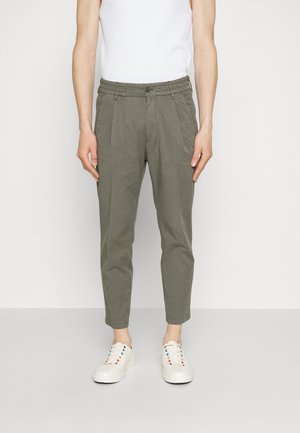 Pantalons khaki fuselés avec plis, en tissu, dotés de poches latérales et d'une fermeture à bouton, associés à des baskets blanches avec des œillets multicolores.